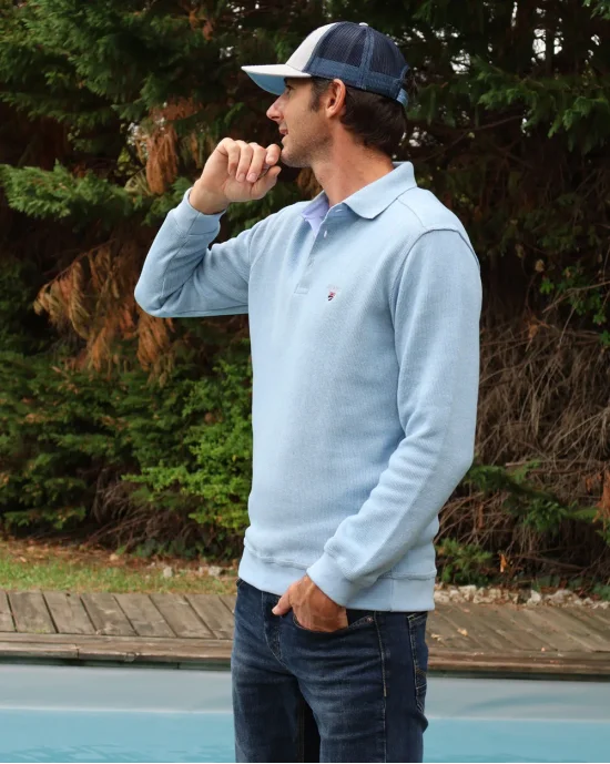 le modèle porte un Polo bleu pastel manches longues pour homme 25POML1 Otago rugby vert ou sweat bleu pastel col polo
